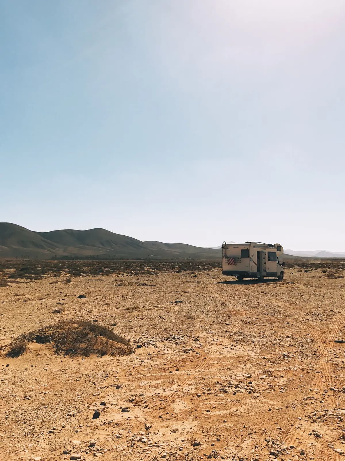 Wohnmobil allein auf einer Wüstenebene auf Fuerteventura, mit Vulkanbergen am Horizont