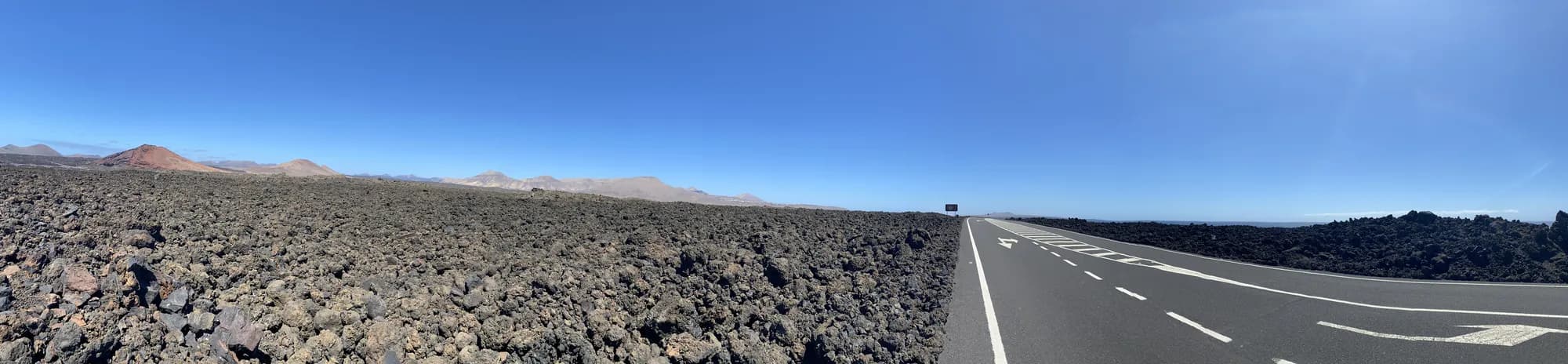 Panoramablick auf eine von Lavafeldern und Vulkanen gesäumte Straße auf Lanzarote