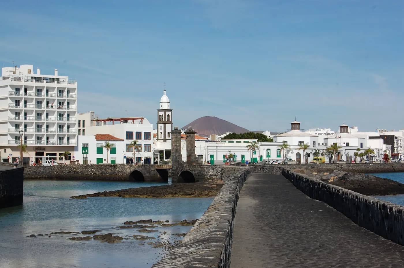 The Puente de las Bolas bridge and the San Ginés church bell tower in Arrecife, with a volcano in the background