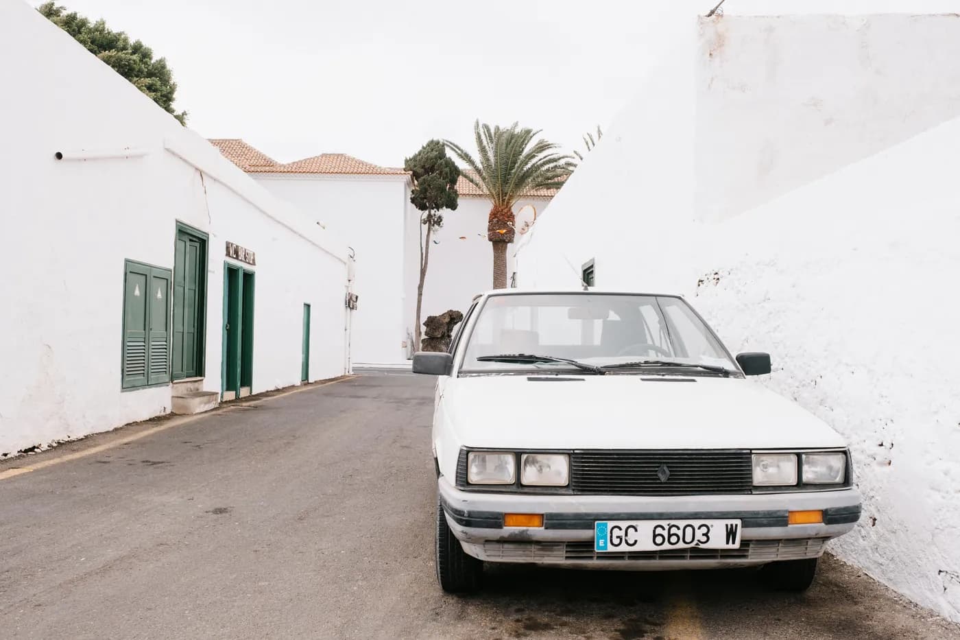 Weiß getünchte Gasse in Teguise mit einem alten Auto vor Häusern mit grünen Fensterläden