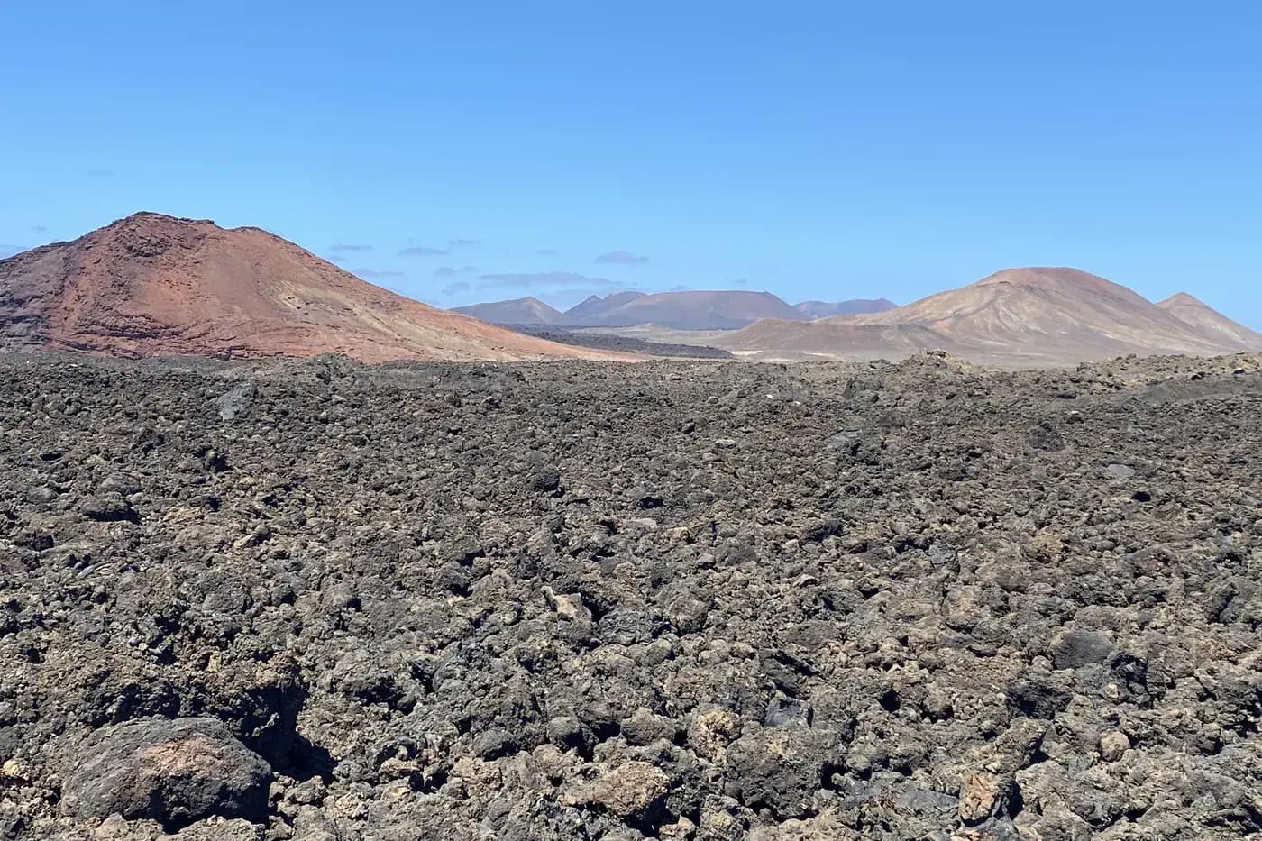 Schwarzes Lavafeld, das sich bis zu bunten Vulkanen erstreckt, auf der Straße nach Los Hervideros