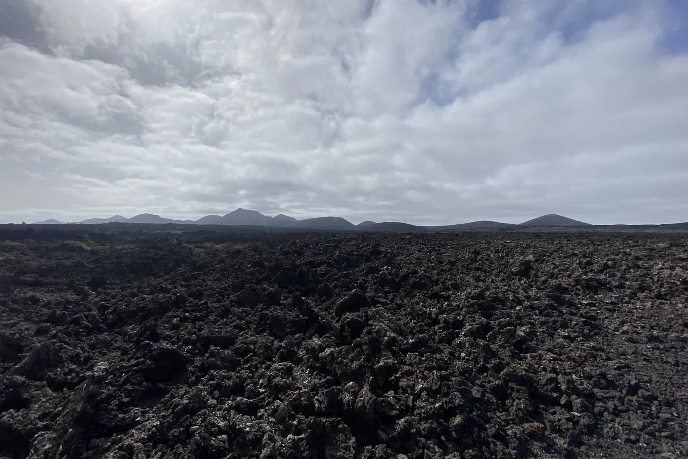 Schwarze Lavaklippen und eine Meereshöhle bei Los Hervideros, im Hintergrund ein roter Vulkan
